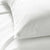A close up of a white Pillowtex Euro Square Size Cotton Pillow Protector on a white bed, machine washable.