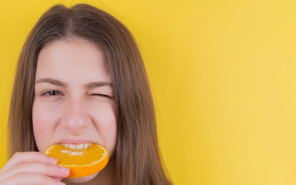 girl holding orange fruit in front of yellow wall